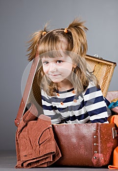 Girl joyfully sits in an old suitcase