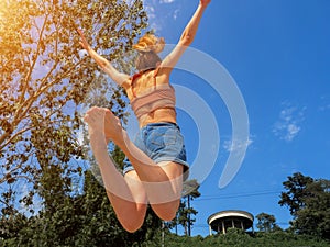 A girl in a jump with her arms spread and her legs curled up against a background of blue sky and green park