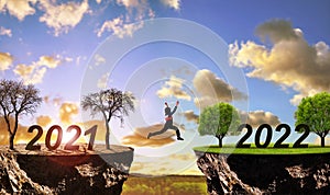 Girl jumping from arid land with number 2021 on lush landscape with number 2022. Concept of Happy New Year.