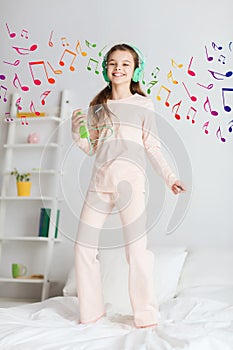 Girl jumping on bed with smartphone and headphones