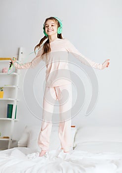 Girl jumping on bed with smartphone and headphones