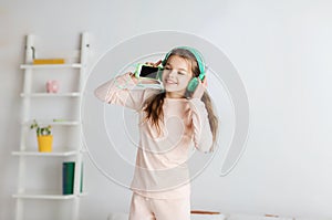 Girl jumping on bed with smartphone and headphones