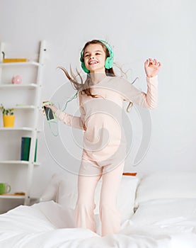 Girl jumping on bed with smartphone and headphones