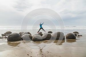 Girl is jumping between boulders at the beach of Moeraki New Zealand