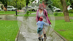 A girl is jumping with a boy in a puddle.