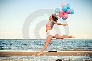 Girl jumping with colorful balloons on beach