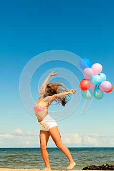 Girl jumping with colorful balloons on beach