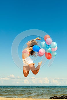 Girl jumping with colorful balloons on beach