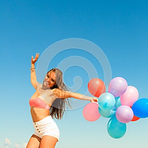 Girl jumping with colorful balloons on beach