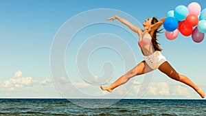 Girl jumping with colorful balloons on beach