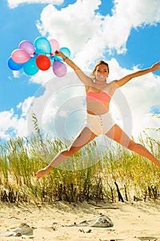 Girl jumping with colorful balloons on beach