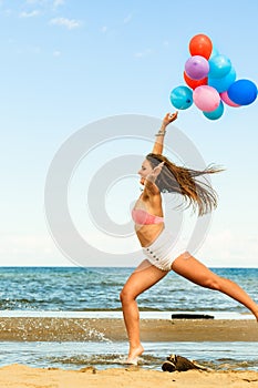Girl jumping with colorful balloons on beach