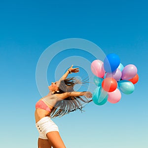 Girl jumping with colorful balloons on sky background