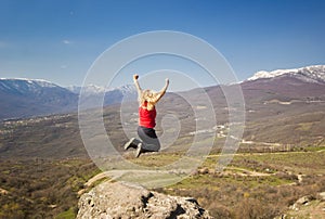 Girl jumping with hands up in the mountains