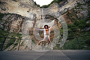 Girl jumping in happiness on mountain waterfall at summer cloudy day time enjoy view with kinchkha waterfall, Georgia. Concept of