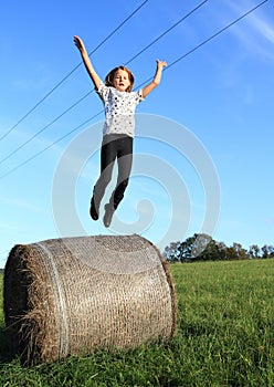 Girl jumping from package of hay