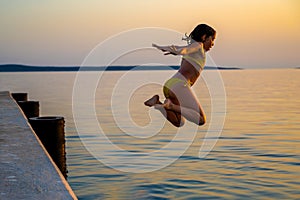 Girl jumping from pier in the water at sunset