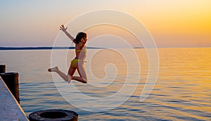 Girl jumping from pier in the water at sunset