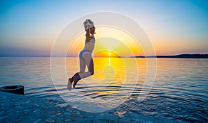 Girl jumping from pier in the water at sunset