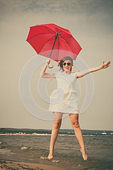 Girl jumping with red umbrella on beach.