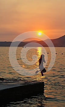 Girl jumping to the water, sunset on Ciovo island in Croatia near Trogir city, Dalmatia
