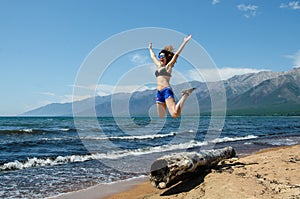 Girl jumping from very old wooden rotten log aground on the beach, near lake Baikal, Russia, on a sunny day in the