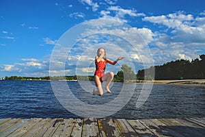 Girl jumping from wooden bridge to water