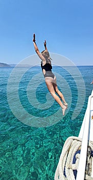 a girl jumps from the side of a yacht into turquoise sea water