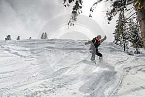 girl jumps with a snowboard from a hill, a springboard with snow, in the mountains against the background of trees