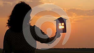 The girl keeps a paper house, dreaming of a large cozy house and a happy family. Silhouette paper houses during sunset.