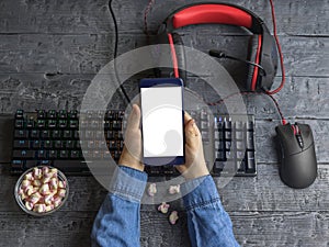 The girl keeps the phone on the background of a desktop with a gaming keyboard, headset and mouse. Clipping background.