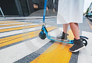 The girl on the electric kick scooter at a pedestrian crossing, legs close-up