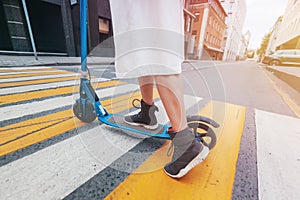 The girl on the electric kick scooter at a pedestrian crossing, legs close-up