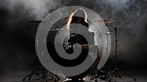 Girl is kicks from playing drums, playing energetic music. Black smoke background. Silhouette