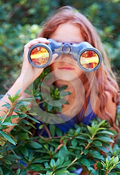 Girl, kid with binoculars and search in nature for learning and fun, forest and adventure at summer camp. Young camper