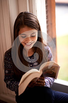 Girl, kid and book with smile in home for reading, learning and language by window for studying. Child, literacy and