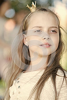 Girl kid on calm face with tiny golden crown on head, nature background, defocused. Girl princess with little crown