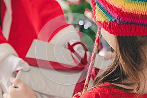 Girl kid holding gift box and red ribbon bow of presents by Santa Claus on Christmas day. Merry Christmas and happy holidays. Girl