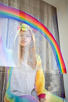 Girl in kigurumi draws rainbow on window. photo