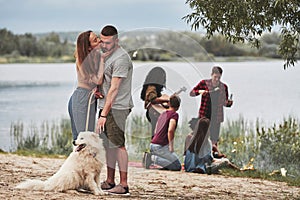 Girl kisses her man. Group of people have picnic on the beach. Friends have fun at weekend time