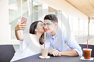 Girl Kissing Boyfriend On Cheek While Taking Selfportrait In Mall photo