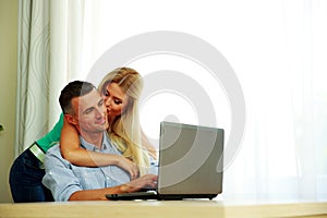 Girl kissing her boyfriend while he using laptop