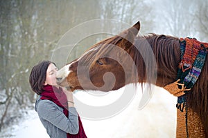 Girl kissing red trakehner stallion horse with scarf in winter