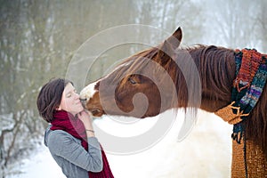 Girl kissing red trakehner stallion horse with scarf in winter