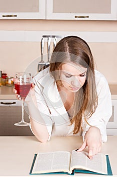 Girl in the kitchen holding a glass and reading book