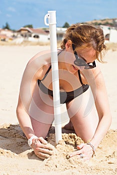 Girl kneeling on the sand puts an beach umbrella
