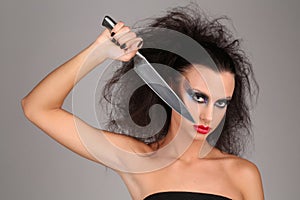 Girl with knifeand wild hair. Close up. Graybackground
