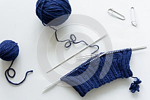 Girl knits blue hat knitting needles on gray wooden background. Process of knitting.