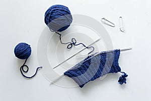 Girl knits blue hat knitting needles on gray wooden background. Process of knitting.