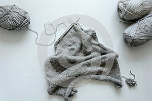 Girl knits gray sweater knitting needles on gray wooden background. Process of knitting